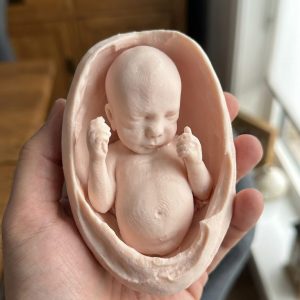 FDM printed fetal keepsake figurine held in hand, natural daylight