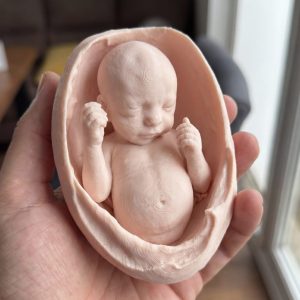 Hand holding a 3D printed fetal keepsake figurine from ultrasound